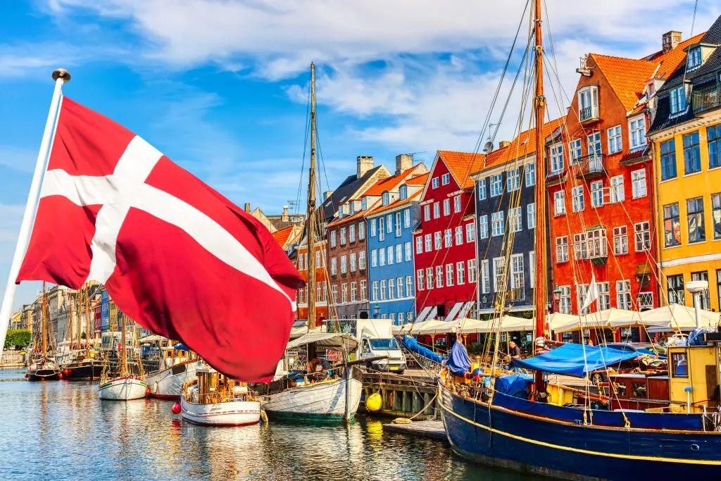 Kopenhagen ikonischen Blick. Berühmte alte Nyhavn Hafen im Zentrum von Kopenhagen, Dänemark im Sommer sonnigen Tag mit Dänemark Flagge im Vordergrund.